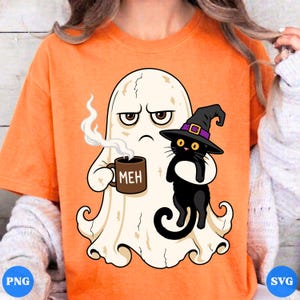 May include: An orange t-shirt featuring a graphic of a white ghost with a grumpy expression holding a brown mug labeled MEH and a black cat wearing a purple-banded witch hat. The ghost has steam rising from the mug, and the cat has yellow eyes.