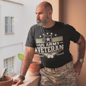 May include: Black t-shirt with "US ARMY VETERAN" text and star graphic. The shirt has a crew neck and short sleeves. The person is wearing camouflage pants and a watch.