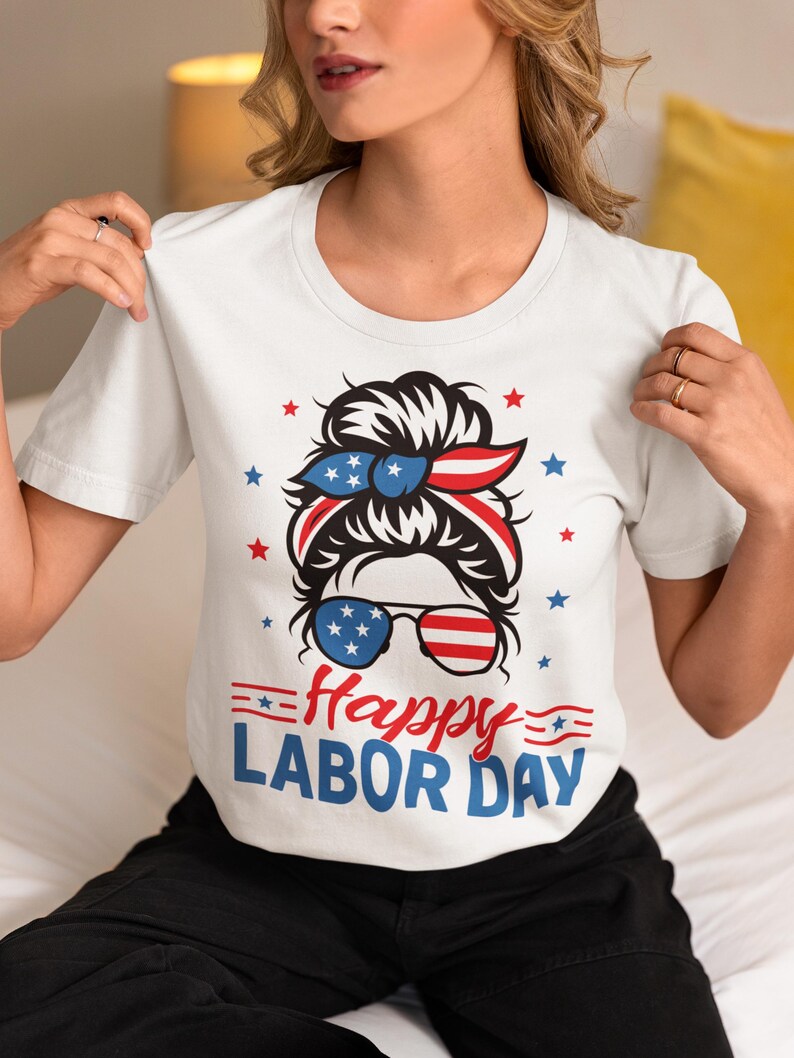 May include: White t-shirt with a graphic design for Labor Day. The design features a woman's face with sunglasses and a headband in red, white, and blue, along with the text "Happy LABOR DAY".