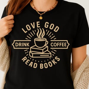 Peut inclure: T-shirt noir avec un motif beige. Le motif comprend les mots "Love God, Drink Coffee, Read Books" autour d'une tasse de café et de livres. Le texte et l'image sont beiges. Le t-shirt est porté par une personne.