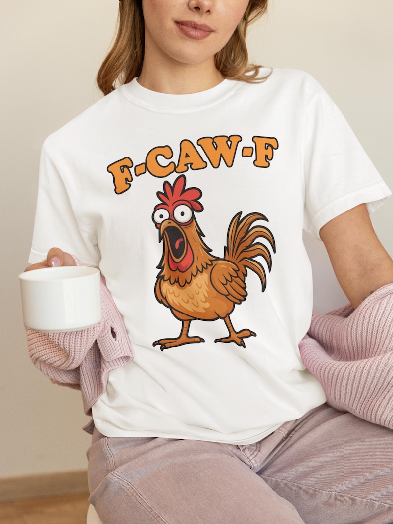 May include: White t-shirt featuring a cartoon chicken with an open beak and the text "F-CAW-F" in orange. The chicken is brown with a red comb and wattle. The shirt is a casual, everyday wear item.