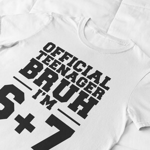 May include: White t-shirt with the text "OFFICIAL TEENAGER BRUH I'M 6+7" in bold black letters. The shirt has a crew neck and short sleeves. The text is arranged diagonally across the front of the shirt.