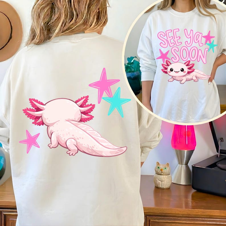 Pu&ograve; includere: Felpa color crema con un'illustrazione di axolotl rosa e stelle rosa e turchesi. L'axolotl &egrave; sul retro della felpa. La parte anteriore della felpa ha il testo "See Ya Soon" con un'illustrazione di axolotl.