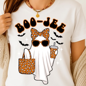 May include: White t-shirt with a Halloween graphic. The design shows a ghost wearing sunglasses and a bow, holding a tote bag and a drink, all with a leopard print pattern. The text "BOO-JIE" is above the ghost.