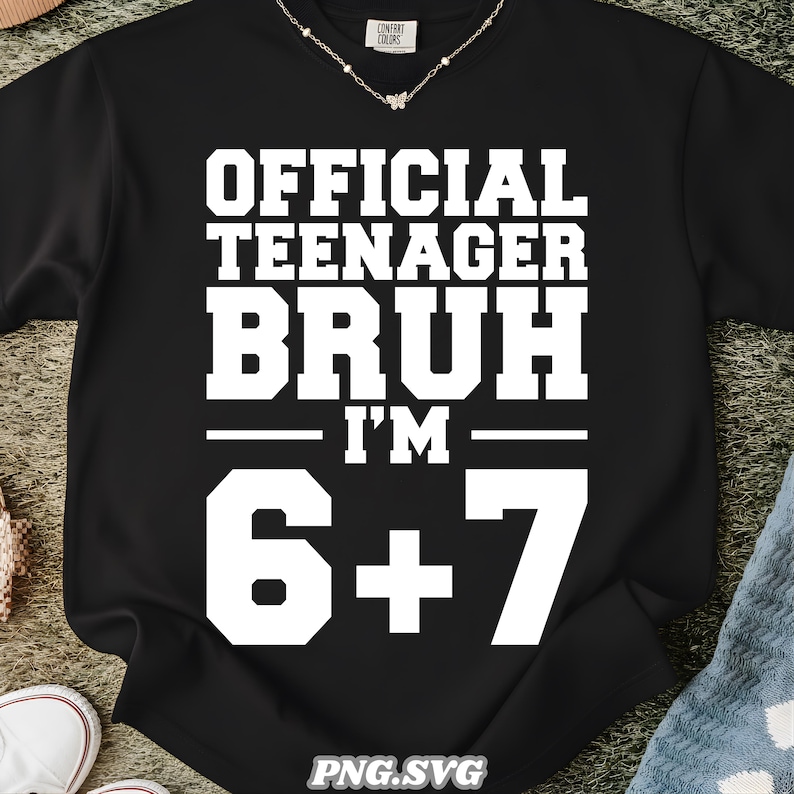 May include: Black sweatshirt with white text that reads "OFFICIAL TEENAGER BRUH I'M 6+7". The sweatshirt has a crew neck and long sleeves. A delicate silver necklace is visible at the neckline.