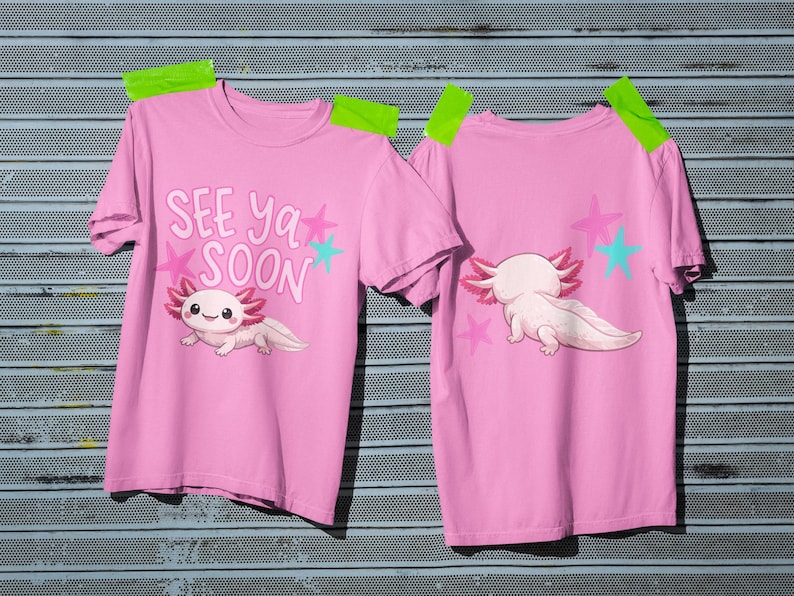 Pu&ograve; includere: Due magliette rosa con un design a cartoni animati di axolotl. Una maglietta mostra il testo "SEE YA SOON" con stelle e un axolotl. L'altra mostra l'axolotl da dietro con stelle. Le magliette sono attaccate a una superficie metallica.