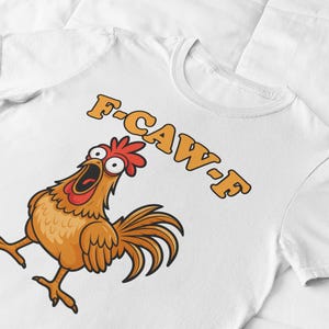 May include: White t-shirt featuring a cartoon chicken with an open beak and the text "F-CAW-F" in orange. The chicken is brown, with a red comb and tail feathers.