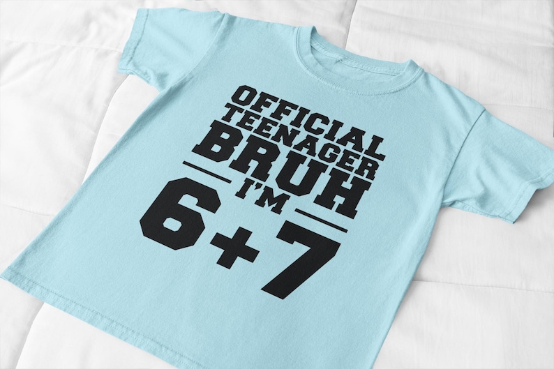 May include: A light blue t-shirt with the text "OFFICIAL TEENAGER BRUH I'M 6+7" in bold black letters. The shirt is made of a soft material and is suitable for casual wear.