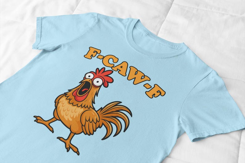 May include: Light blue t-shirt featuring a cartoon chicken with an open beak and the text "F-CAW-F" in orange. The chicken is brown, with a red comb and tail feathers. The shirt is made of a soft material.