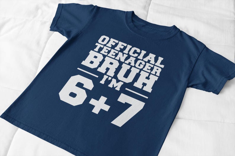 May include: A navy blue t-shirt with the text "OFFICIAL TEENAGER BRUH I'M 6+7" in white block letters. The shirt is made of a soft material and is suitable for casual wear. The text is centered on the front of the shirt.