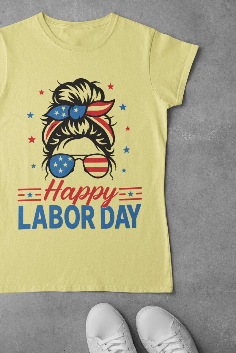 May include: Yellow t-shirt with a graphic design for Labor Day. The design features a woman's face with sunglasses and a headband in red, white, and blue. The text "Happy Labor Day" is below the face.