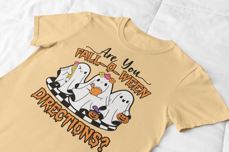 K&ouml;nnte beinhalten: Hellgelbes T-Shirt mit einem Halloween-Motiv. Das Design zeigt drei Cartoon-Geister mit Accessoires und dem Text "Are You Fall-O-Ween Directions?". Die Geister stehen auf einer schwarz-wei&szlig; karierten Plattform.