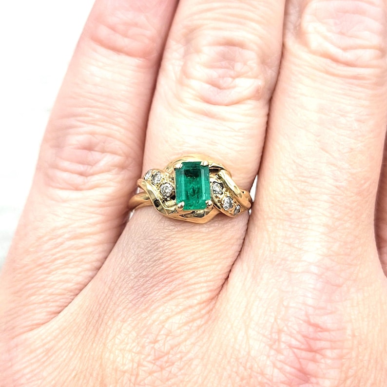 Vintage Emerald Ring in 14k Yellow Gold with Diamonds. Lucious medium Green Emerald cut Emerald makes a Statement in an Art Nouveau-esque Setting. Not too big or too small this half-carat size gemstone is a beautiful sample of Natural Emerald sure to Complement any Outfit.
