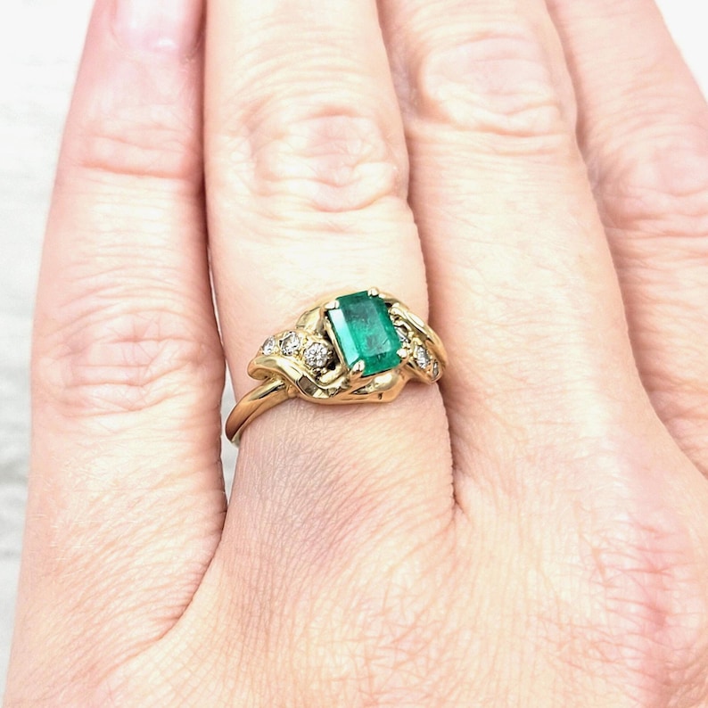 Vintage Emerald Ring in 14k Yellow Gold with Diamonds. Lucious medium Green Emerald cut Emerald makes a Statement in an Art Nouveau-esque Setting. Not too big or too small this half-carat size gemstone is a beautiful sample of Natural Emerald sure to Complement any Outfit.