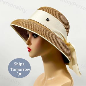 May include: A wide-brimmed straw hat with a white ribbon and bow. The hat has a brown and white striped pattern.