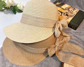 May include: Two straw sun hats with wide brims and brown ribbon bows. The hats are stacked on top of each other. A pair of white sunglasses with black lenses is in the foreground.