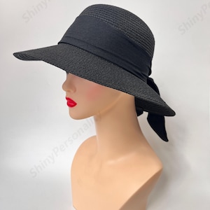 May include: A black wide-brimmed sun hat with a black ribbon tied at the back. The hat is made of a woven straw-like material.