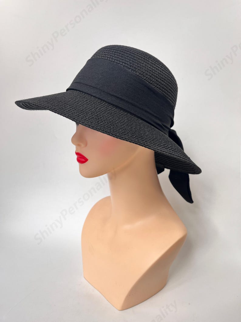 May include: A black wide-brimmed sun hat with a black ribbon tied at the back. The hat is made of a woven straw-like material.