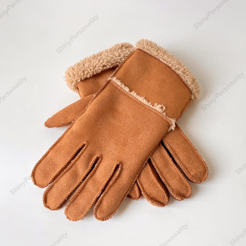 May include: A pair of brown gloves with a soft, suede-like texture. The gloves have a plush, tan-colored trim around the wrist area. The gloves are designed with individual finger slots and are likely intended for cold weather.