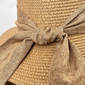 May include: A straw sun hat with a wide brim and a brown fabric ribbon tied in a bow at the crown.