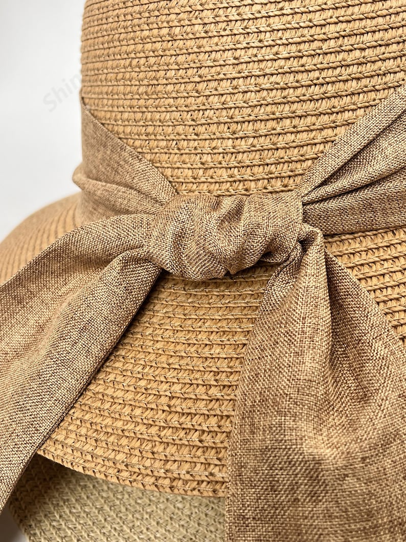 May include: A straw sun hat with a wide brim and a brown fabric ribbon tied in a bow at the crown.