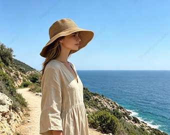 May include: A beige linen dress with a V-neckline and three-quarter length sleeves, paired with a wide-brimmed tan straw hat featuring a ribbed texture. The garment has a gathered waistline and a flowing skirt, presented in a natural outdoor setting.