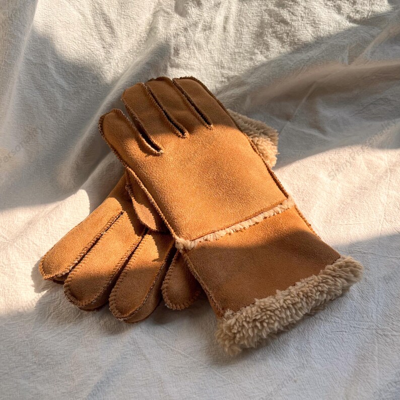 May include: A pair of tan gloves made of suede-like material with a soft, fuzzy lining. The gloves have a classic design with individual fingers and a warm, cozy appearance, perfect for cold weather.