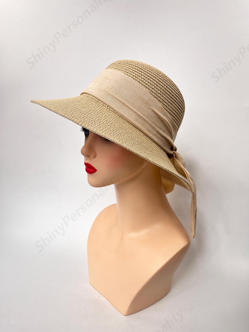 May include: A wide-brimmed straw hat with a beige ribbon tied around the crown. The hat is on a white mannequin head.
