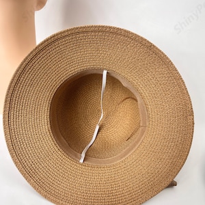 May include: A brown straw sun hat with a white ribbon tied around the crown. The hat is made of woven straw and has a wide brim.