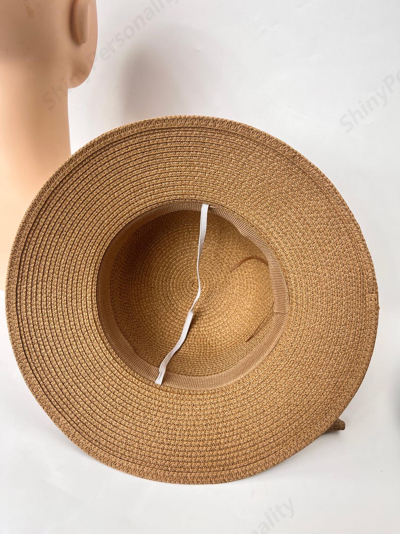 May include: A brown straw sun hat with a white ribbon tied around the crown. The hat is made of woven straw and has a wide brim.