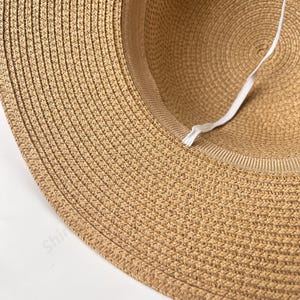 May include: A close-up of the underside of a brown straw hat. The hat has a white elastic band sewn into the inside of the hat.