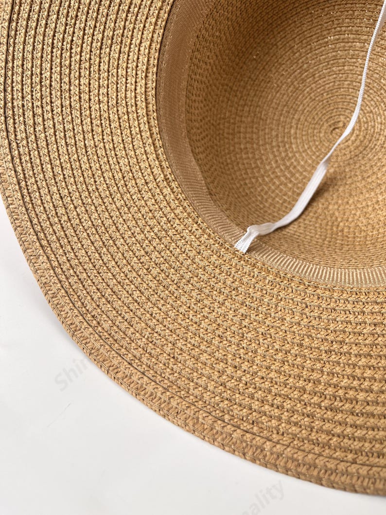 May include: A close-up of the underside of a brown straw hat. The hat has a white elastic band sewn into the inside of the hat.