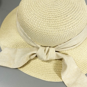 May include: A beige straw sun hat with a wide brim and a large bow made of the same material.