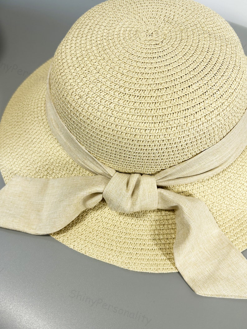 May include: A beige straw sun hat with a wide brim and a large bow made of the same material.