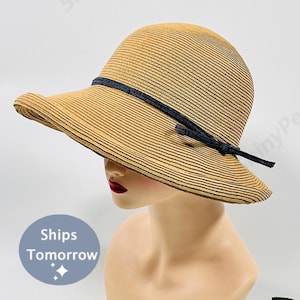 May include: A wide-brimmed straw hat with a black ribbon and bow. The hat has a striped pattern and is a light brown color.