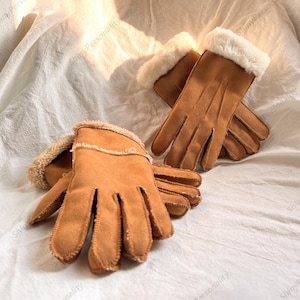 May include: A pair of brown gloves with a soft, suede-like texture. The gloves have a white, fluffy trim around the cuffs. The gloves are designed for warmth and comfort, perfect for cold weather.