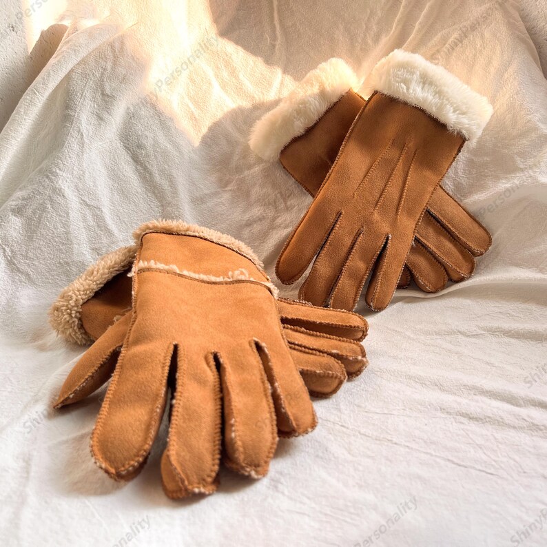 May include: A pair of brown gloves with a soft, suede-like texture. The gloves have a white, fluffy trim around the cuffs. The gloves are designed for warmth and comfort, perfect for cold weather.