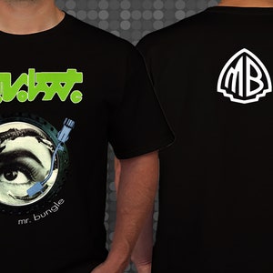 Puede incluir: Camiseta negra con un logotipo verde de "Mr. Bungle" y un gráfico de un ojo en un tocadiscos. La parte posterior de la camiseta tiene un logotipo blanco de "MB".