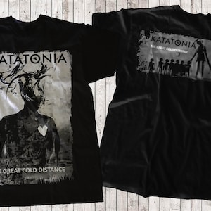 May include: Black t-shirt with a white graphic print of a band called Katatonia. The front of the shirt features a black and white image of a person with a heart on their chest. The back of the shirt features the band's name and the album title "The Great Cold Distance".
