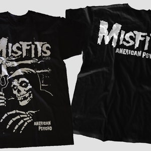 May include: Black t-shirt with a white graphic of a skeleton wearing a hooded robe and holding a trident. The text "Misfits" and "American Psycho" are printed on the shirt.