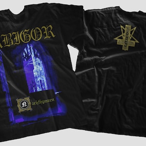 Peut inclure: T-shirt noir avec un imprimé doré du groupe Abigor. Le devant du t-shirt présente une image de style gothique d'un bâtiment avec le texte "archthrymmen". Le dos du t-shirt présente un pentagramme doré avec le nom du groupe au centre.