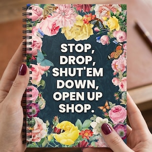 May include: A spiral-bound notebook with a floral design and the text "STOP, DROP, SHUT'EM DOWN, OPEN UP SHOP." The cover features a dark blue background with a border of pink, yellow, and white flowers and butterflies.