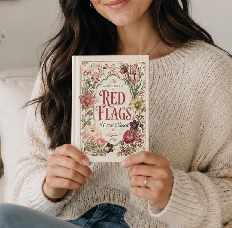 May include: A hardcover book titled A Little Book of Red Flags I Chose to Ignore Again. The cover is cream-colored with a decorative gold border and a vibrant floral illustration featuring pink, red, and green flowers surrounding the red text.