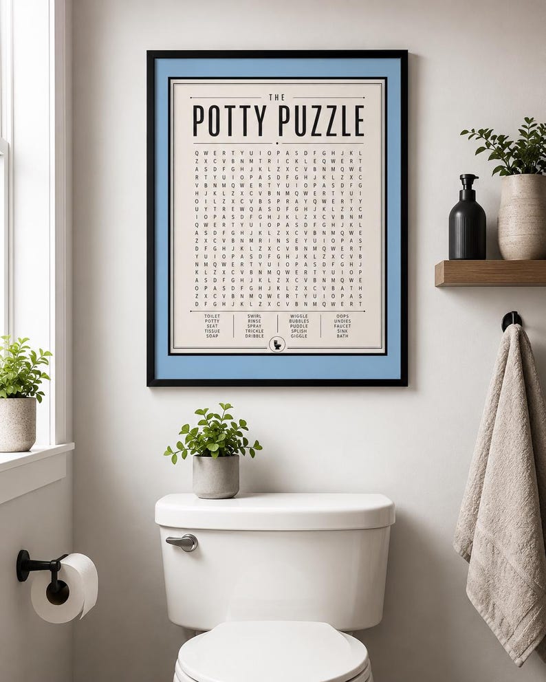 K&ouml;nnte beinhalten: Ein gerahmter Wandkunstdruck mit dem Titel The Potty Puzzle, der ein Wortsuchr&auml;tsel mit schwarzem Text auf cremefarbenem Hintergrund zeigt, eingefasst in ein hellblaues Passepartout und einen d&uuml;nnen schwarzen Rahmen mit Wortliste und WC-Symbol.