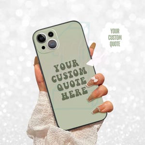 Puede incluir: Una funda de teléfono verde salvia con un borde negro. La funda presenta el texto "YOUR CUSTOM QUOTE HERE" en una fuente retro. Una burbuja de texto blanca a la derecha dice "YOUR CUSTOM QUOTE".