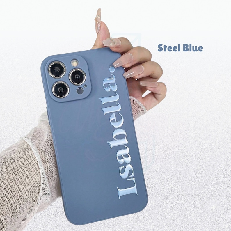May include: Steel blue phone case featuring the name "Isabella" in a vertical, raised, silver font. The case has a matte finish and a camera module with three lenses. The text "Steel Blue" is in the upper right corner.