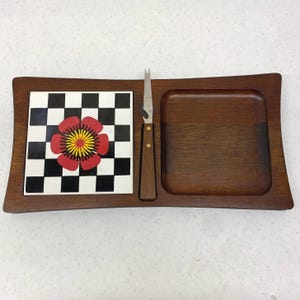 May include: A wooden serving tray with a checkerboard tile featuring a red and yellow flower design. Includes a cheese knife and a recessed area for serving. The tray is a warm brown color.