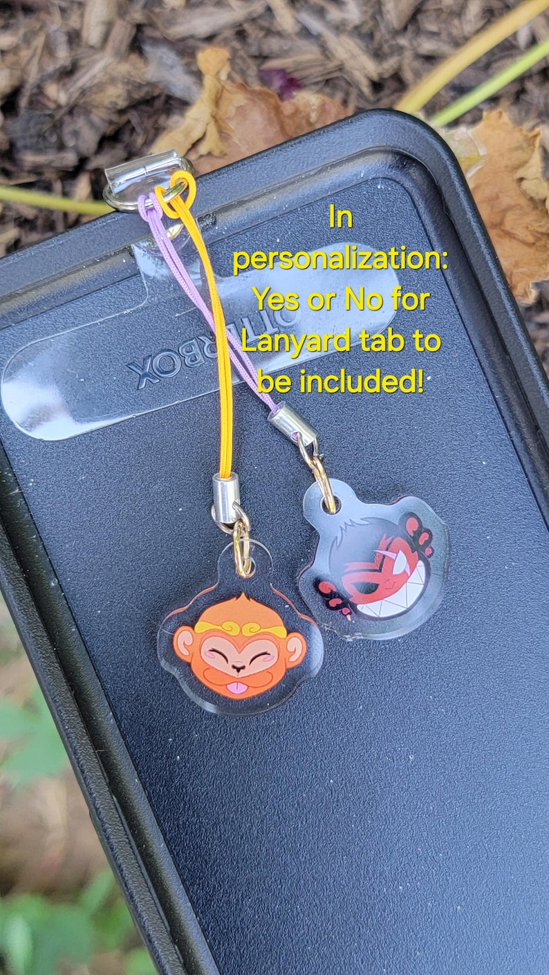 May include: Two colorful phone charms with cartoon monkey and demon faces.  The charms are attached to a black phone case with a lanyard tab.  In personalization: Yes or No for Lanyard tab to be included!