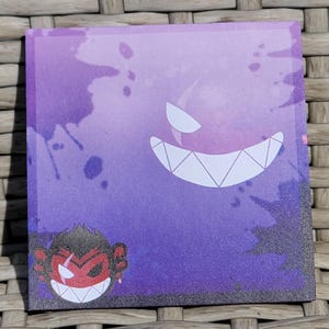 Puede incluir: Adhesivo cuadrado con fondo morado y negro con un fantasma de dientes blancos y un mono de cara roja con un pendiente rojo. El adhesivo tiene una textura brillante.