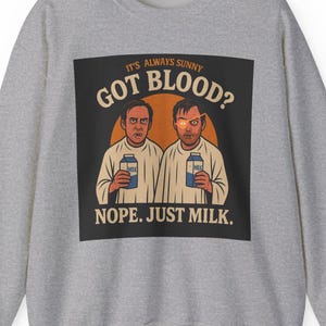 May include: A heather gray sweatshirt featuring a graphic from the show "It's Always Sunny in Philadelphia." The graphic reads "GOT BLOOD?" above two cartoon figures holding milk cartons, with the text "NOPE. JUST MILK." below.